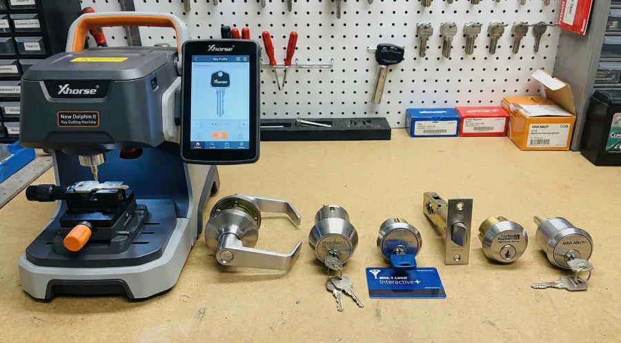 An Xhorse XP-005L Dolphin II key cutting machine on a locksmith workbench in McKinney, TX, displayed alongside high-security commercial locks from Schlage, Medeco, Mul-T-Lock, Yale, and Corbin Russwin.