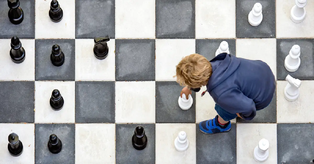 Child playing outdoor chess on a big board