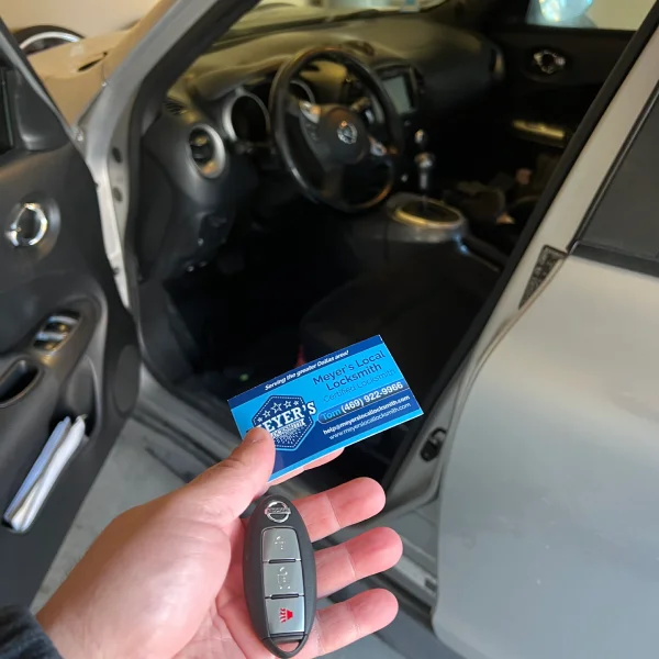 Locksmith holding a new key beside a silver sedan with the driver door open after a car lockout